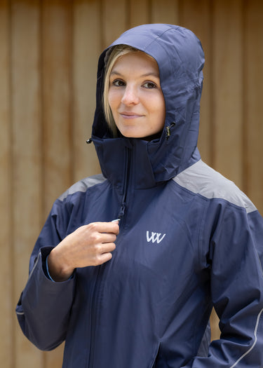 Person wearing a navy raincoat with a hood, standing against a wooden wall.