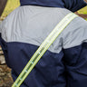 Person wearing a navy jacket with reflective stripes, wearing an LED sash standing next to a horse.