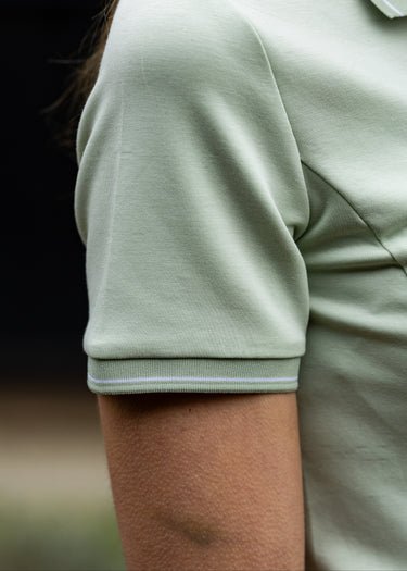 Close-up of a person wearing a light green polo shirt with a blurred background