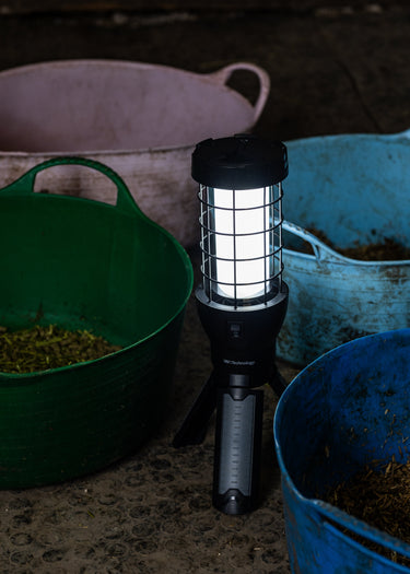 Portable lantern emitting light on a dark surface with buckets in the background