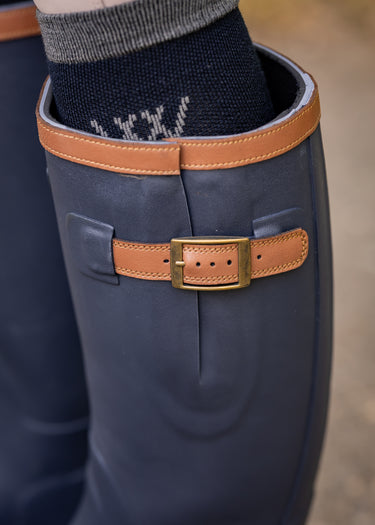 Close-up of a blue rubber boot with a brown leather strap and buckle on a blurred background